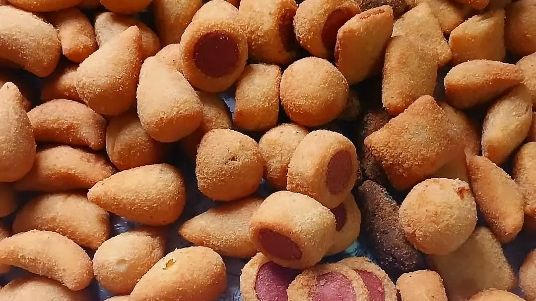 Salgados fritos misturados de perto: coxinhas, bolinhas de queijo, croquetes e enrolados de salsicha, um deles cortado mostrando a salsicha